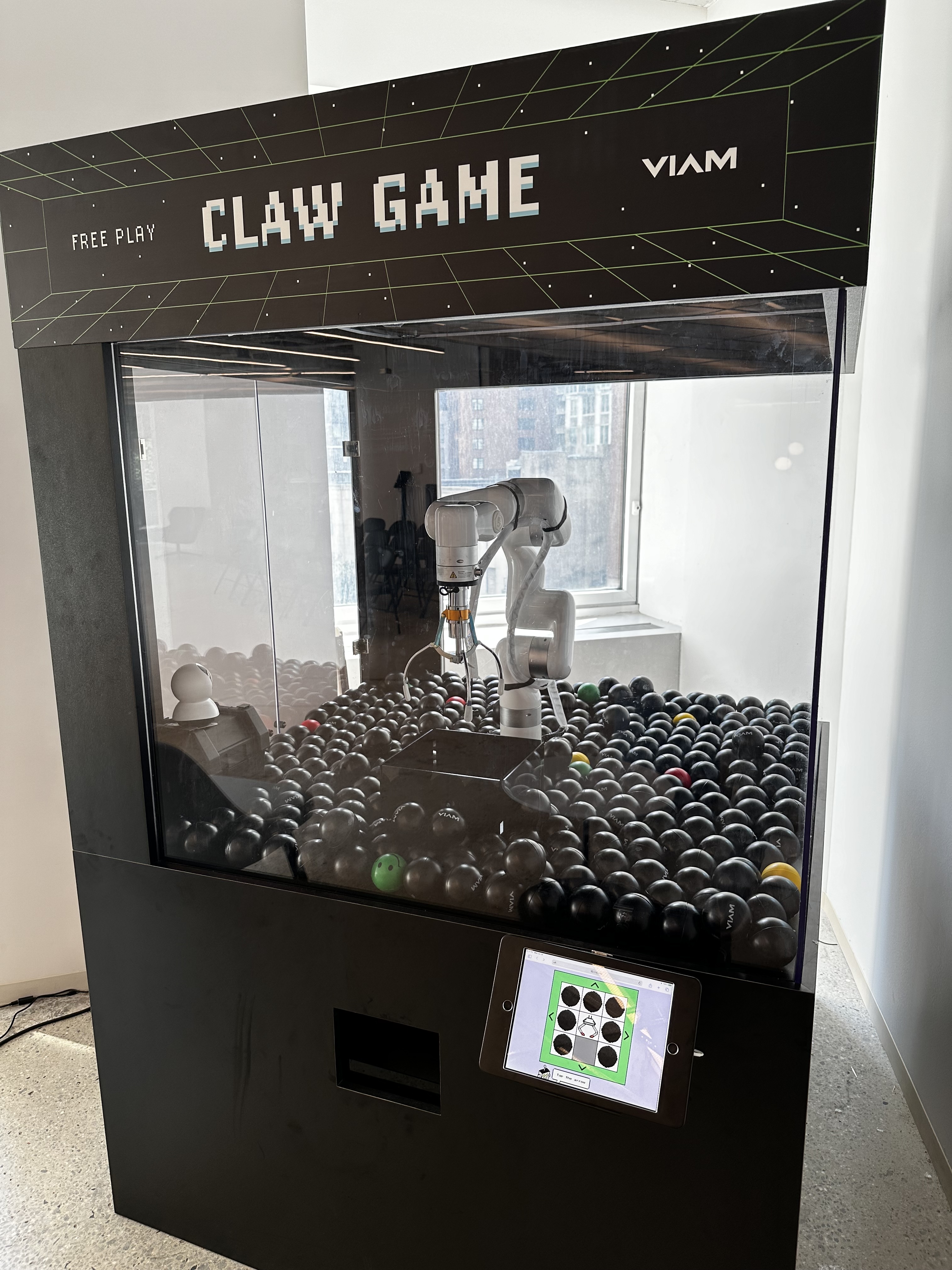 a large arcade cabinet full of black, red, and green balls surrounding a robotic arm with an arcade claw attached at tehe top end